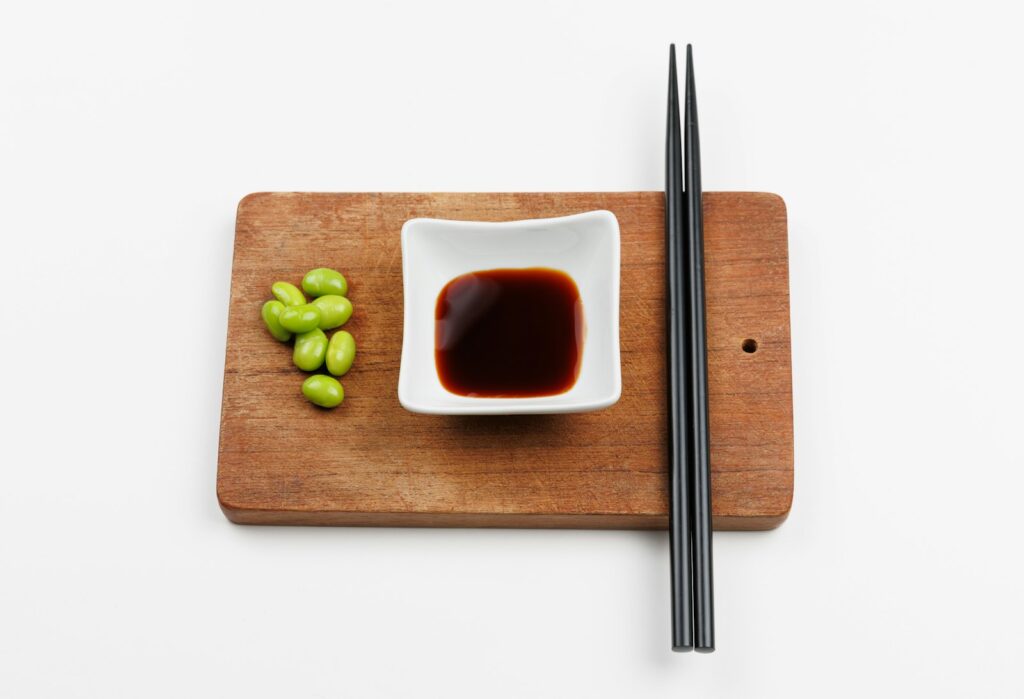 A chopping board with chopsticks and a small bowl of sauce
