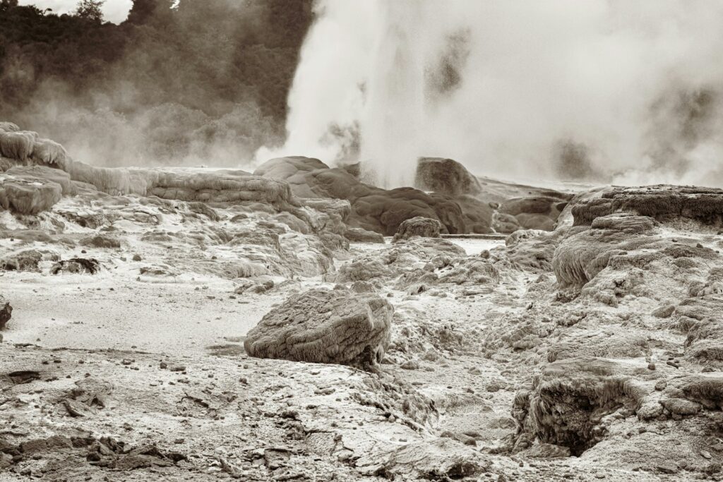 A geyser erupting with steam amidst rocky, barren terrain