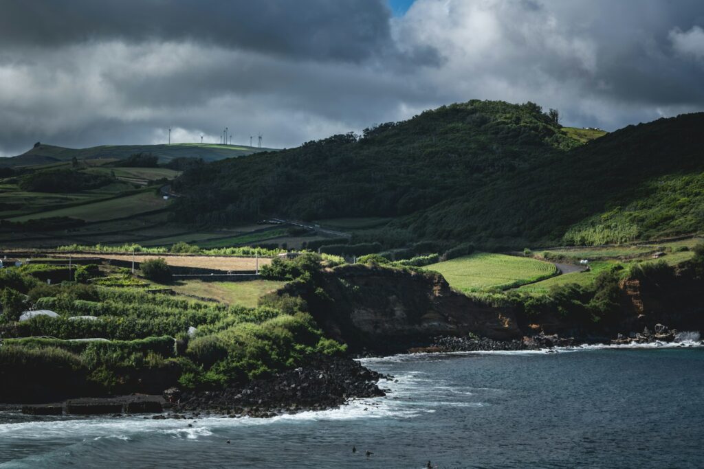Green rolling hills meet the dark ocean under cloudy skies