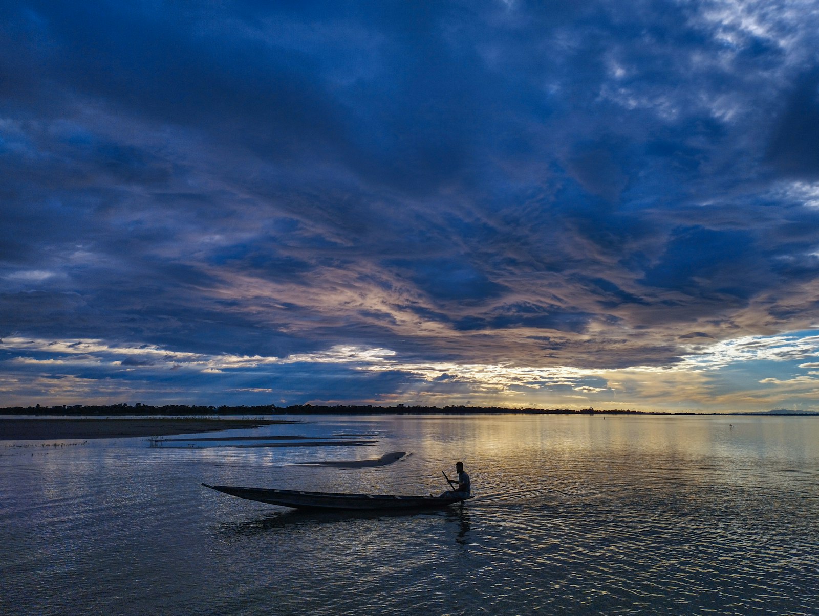 A lone fisherman rows a boat at sunset