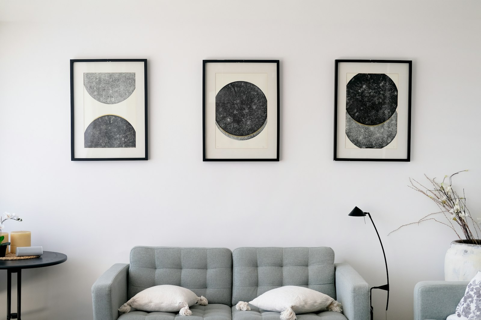 Three abstract art pieces hang above a gray sofa
