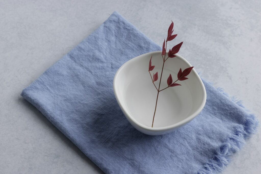 A white bowl with red plant on a blue cloth