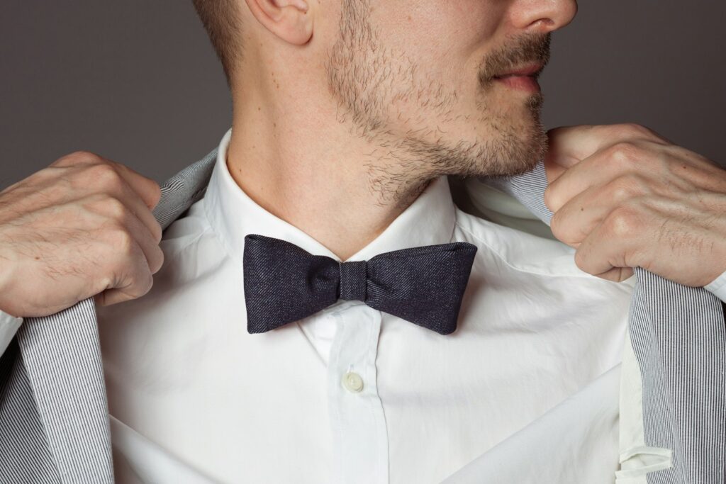 Man adjusting his grey suit jacket and dark bow tie