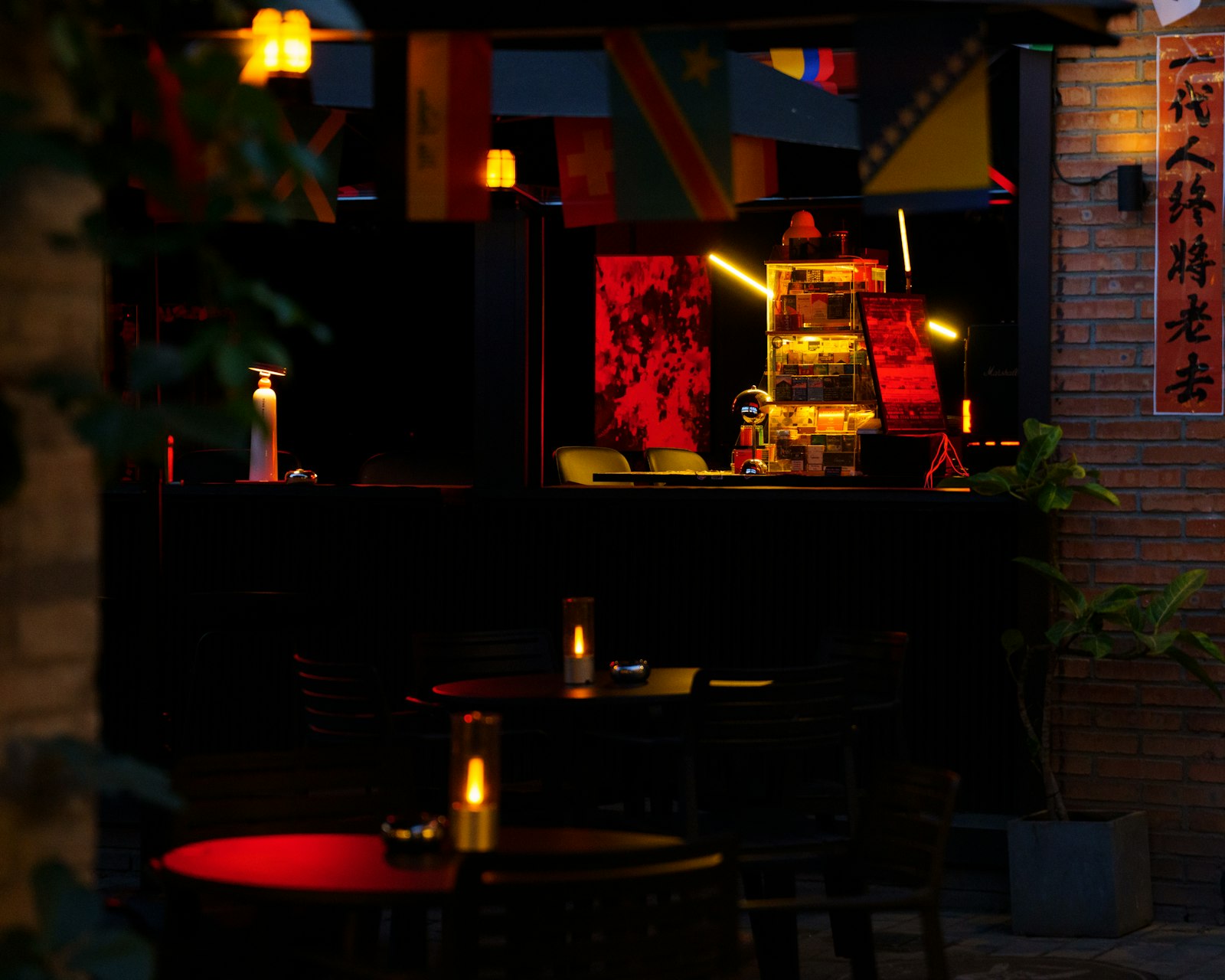 Dark outdoor cafe with illuminated red tables and building lights