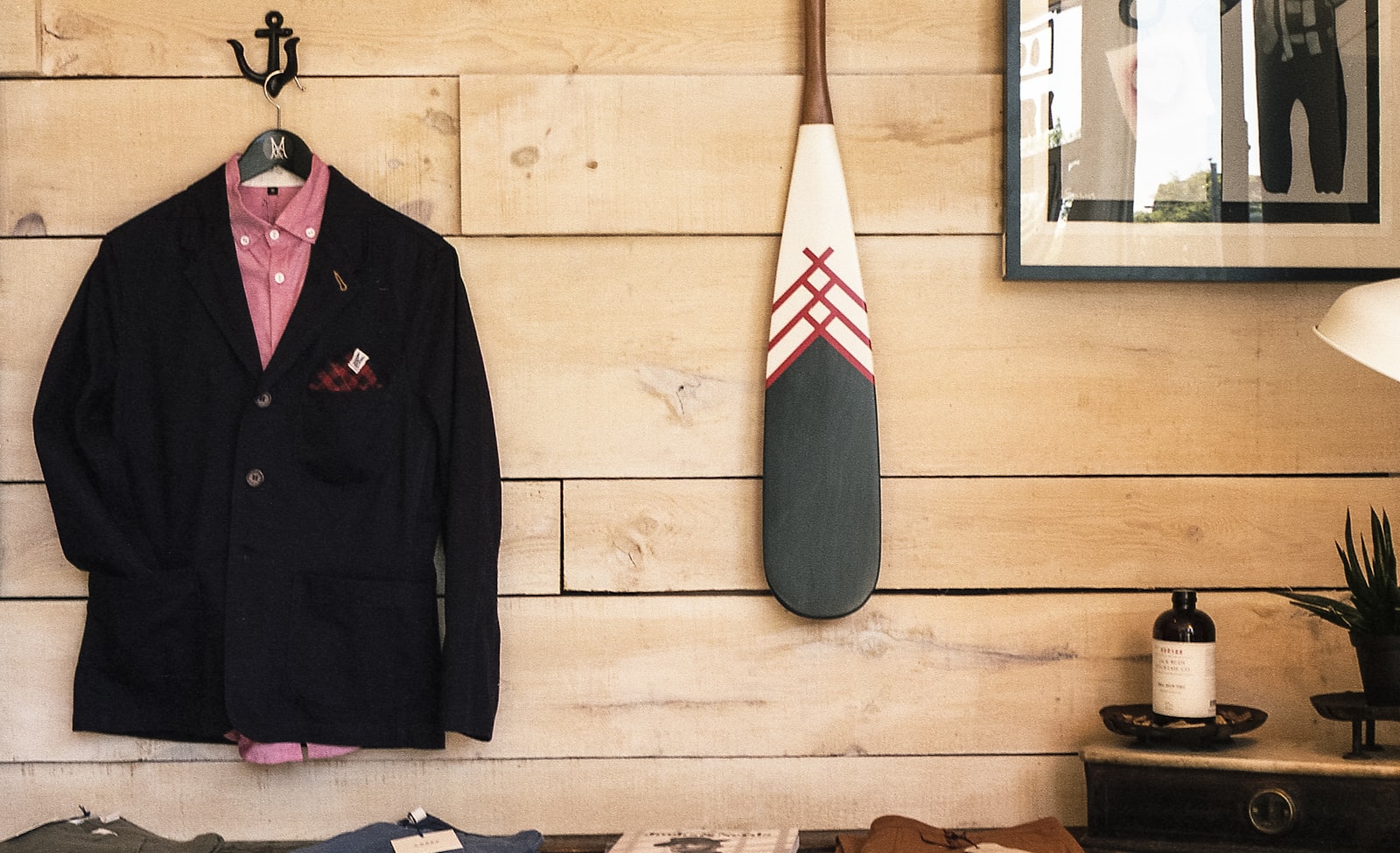Black jacket hanging on brown wooden wall beside boat paddle