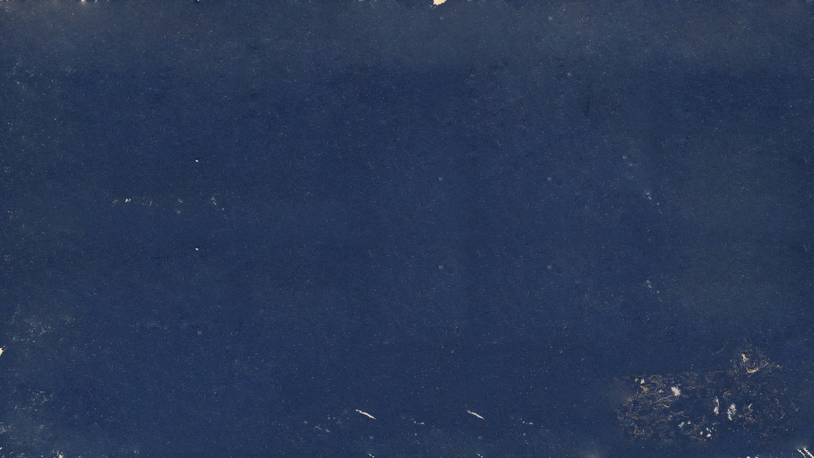 A dark blue textured surface with subtle light specks and worn edges