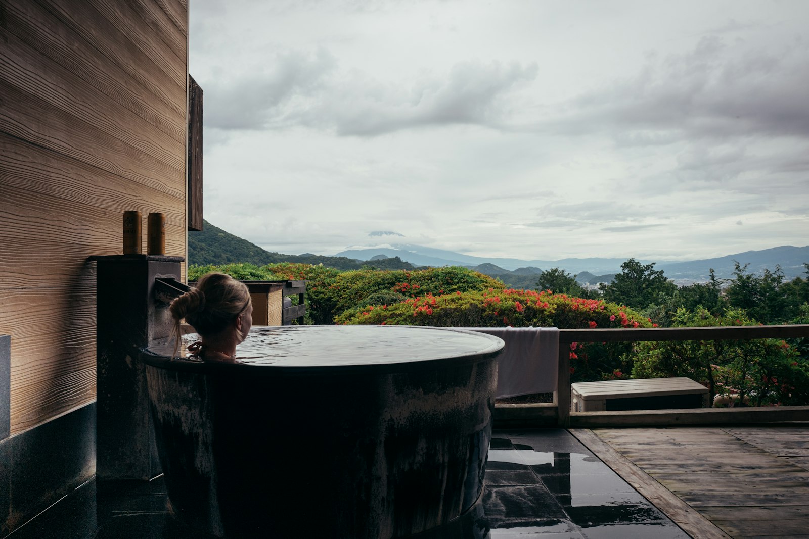 Woman relaxing in an outdoor wooden bathtub with mountain view