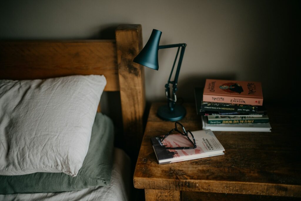 A stack of books sitting on top of a bed next to a lamp