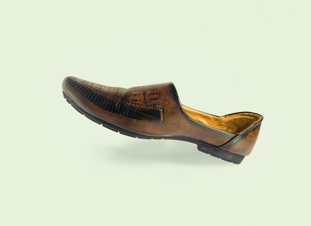 A brown leather loafer with perforated details on a light background