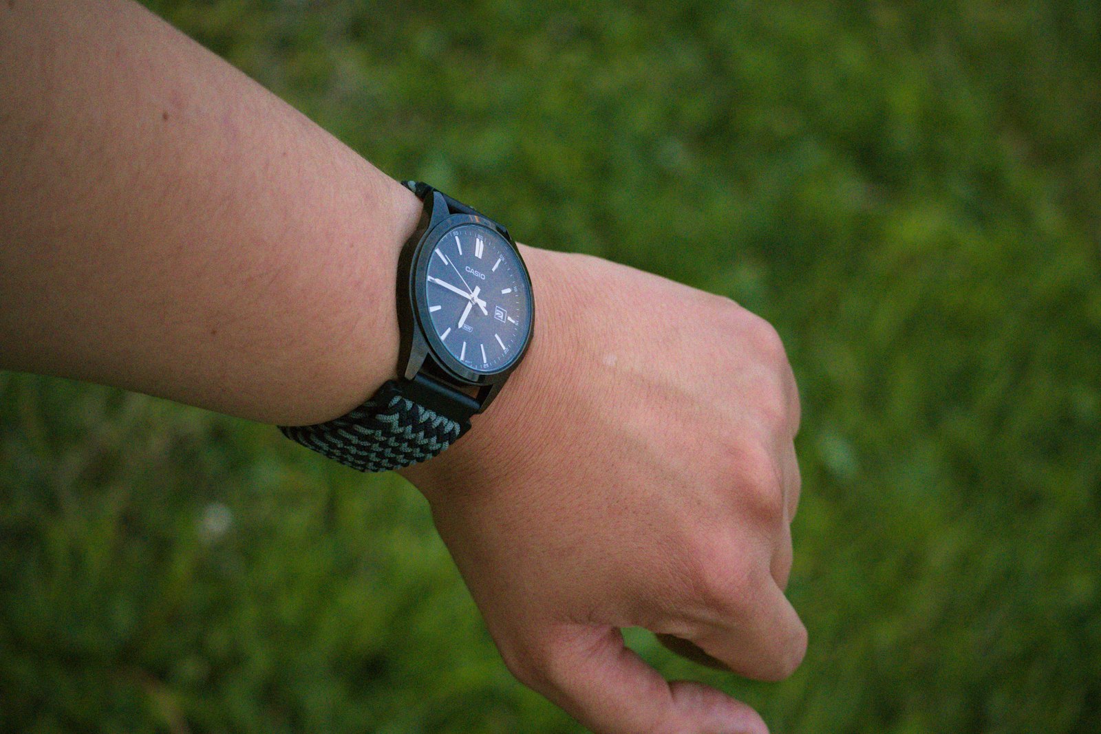 A person's arm wearing a black watch against green grass