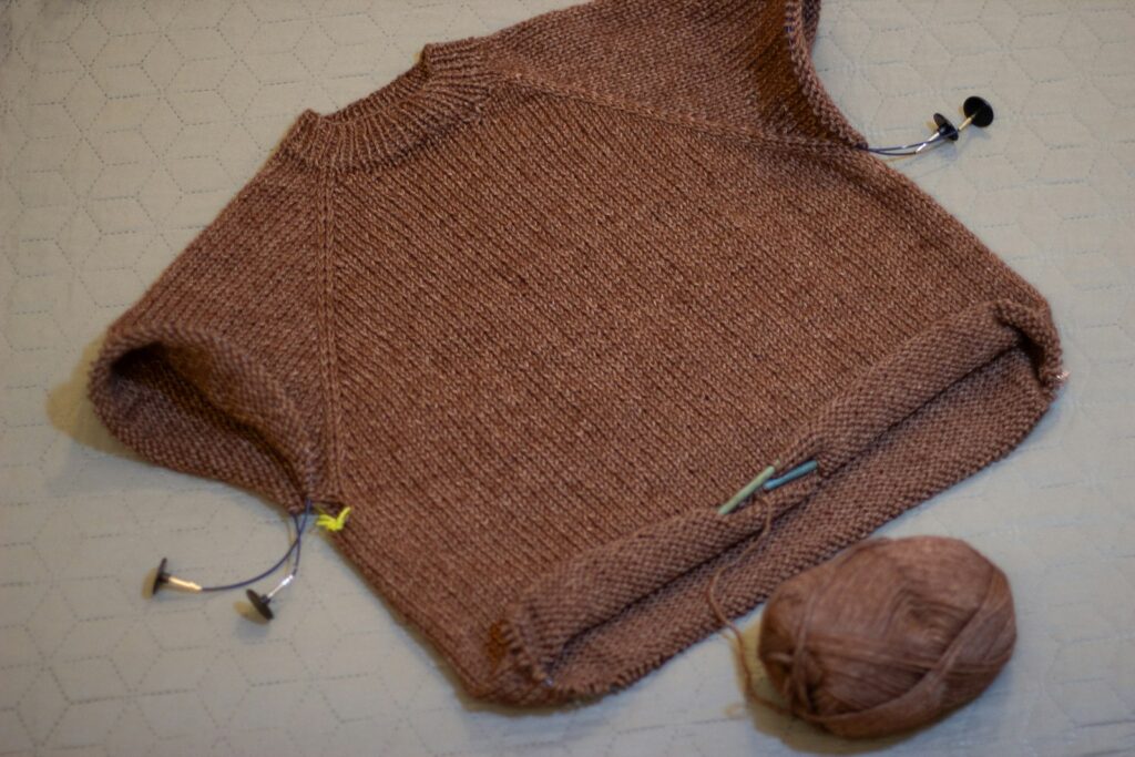 Knitted brown sweater with stitch markers and yarn ball