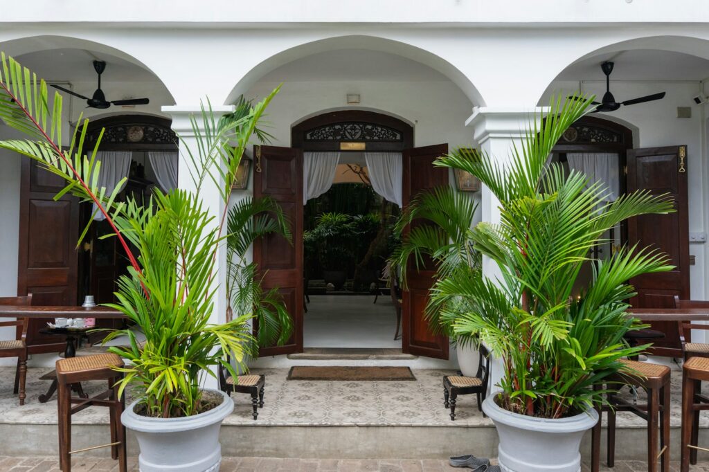 White building entrance with arched doorways and potted palm plants