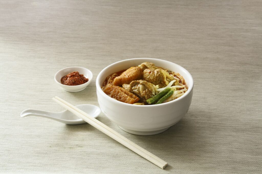 White ceramic bowl filled with cooked noodles near white chopsticks