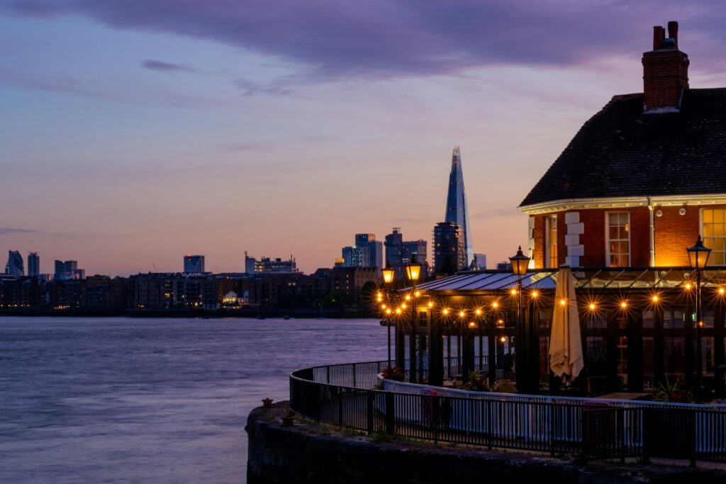 Illuminated riverside pub with london city skyline at twilight