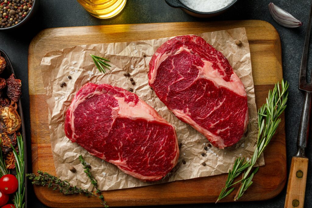 Two steaks on a cutting board with herbs and spices