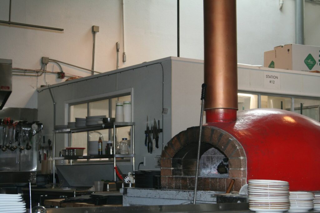 A commercial kitchen features a large red brick pizza oven