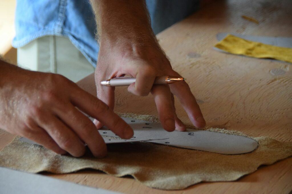 A person tracing a paper shoe pattern onto a piece of leather