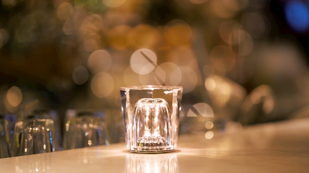 Lit candle in glass holder on bar with warm bokeh
