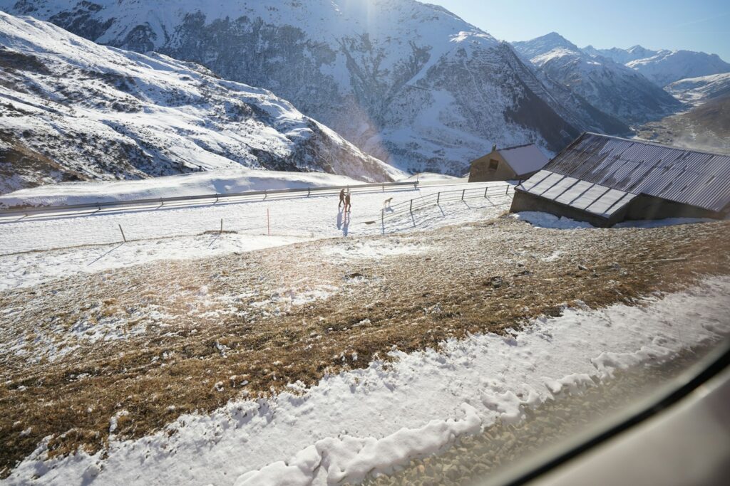 Snowy mountain road with rustic buildings and sun glare