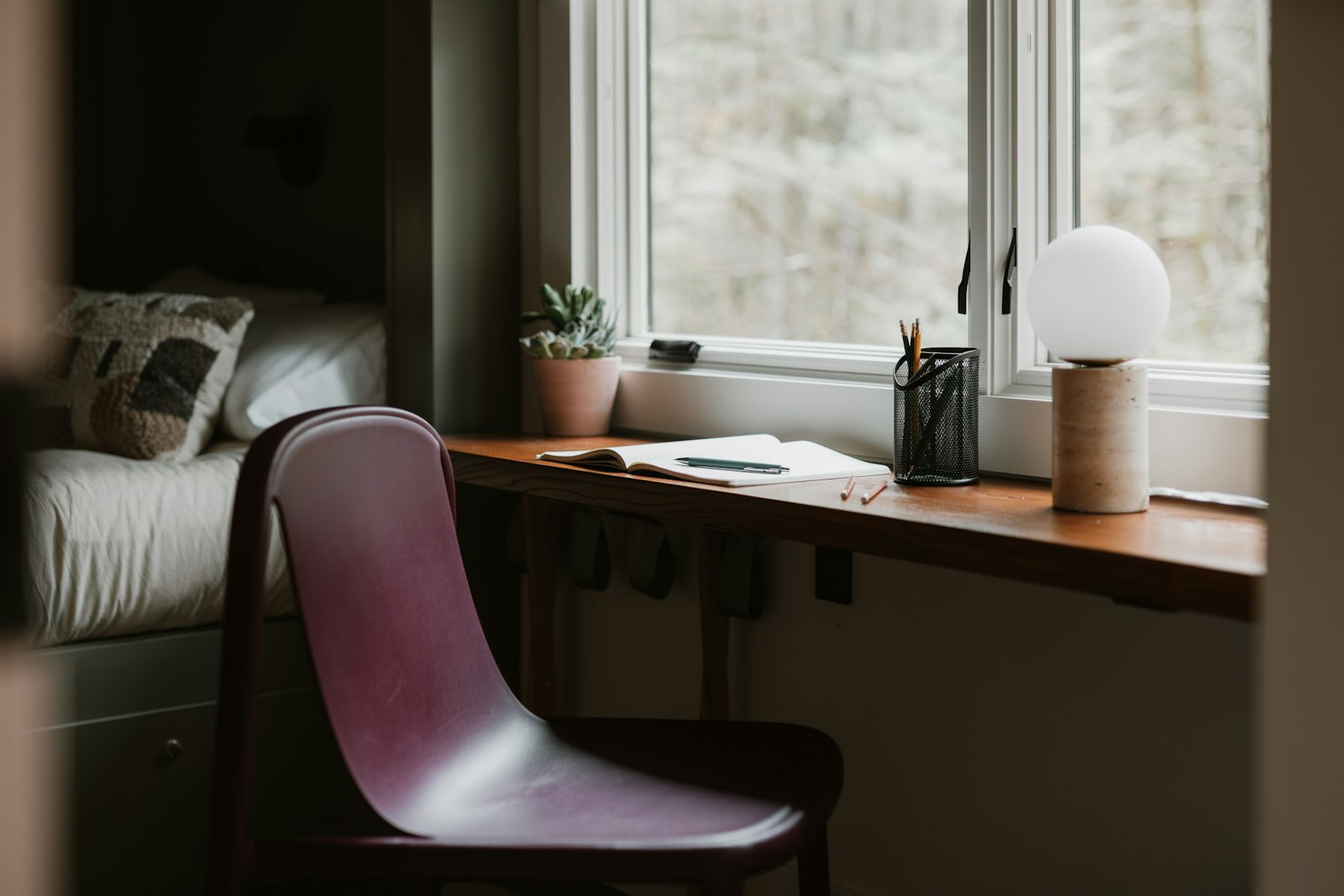 A chair and desk by a window with a lamp