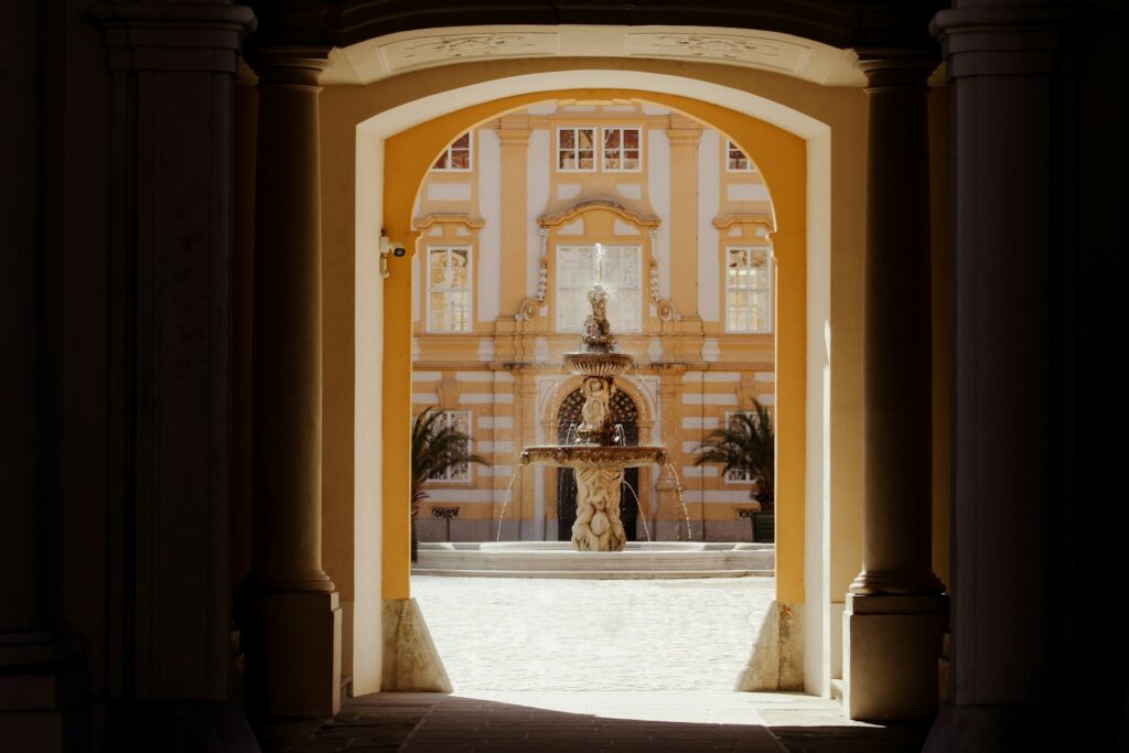 Ornate building and fountain seen through a sunlit archway