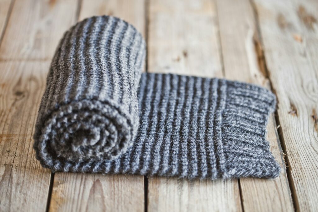 A gray and white knitted blanket laying on top of a wooden floor
