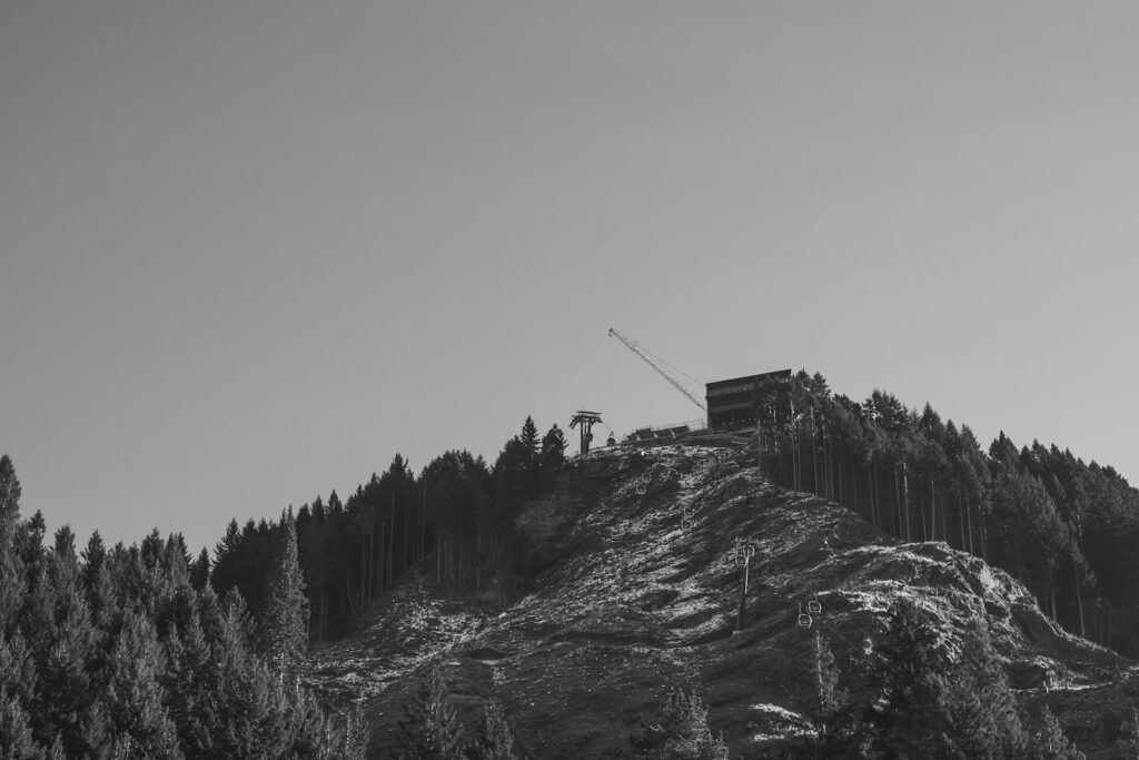 A construction crane on a mountain peak above a dense pine forest