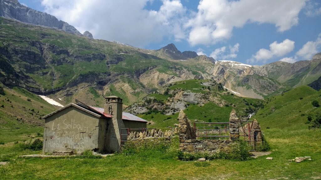 Gray concrete house on green grass field near mountain under white clouds during daytime