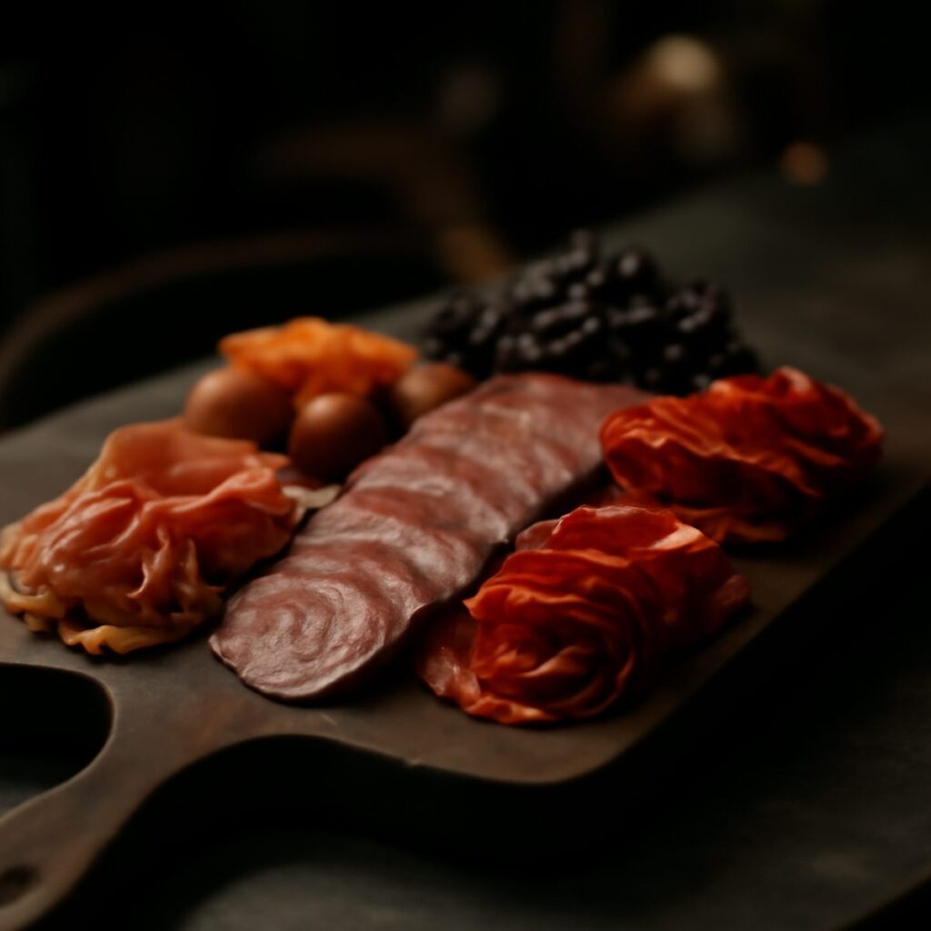 Wooden board with sliced cured meats, cheese, and garnishes