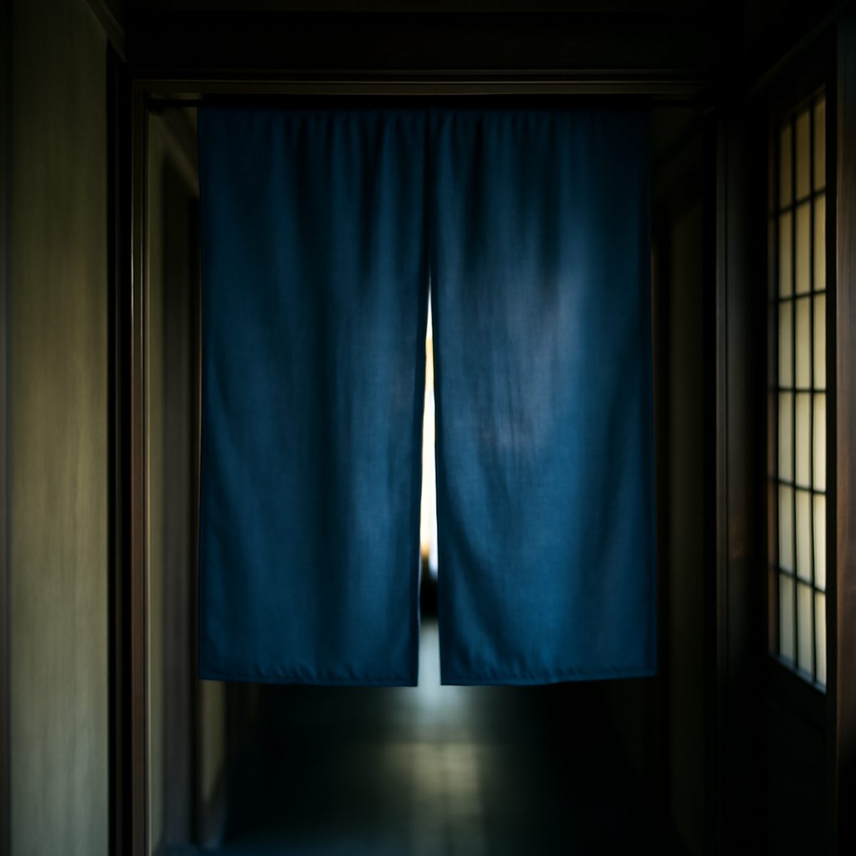 Indigo split noren curtain hanging in a doorway, moving softly in low calm light